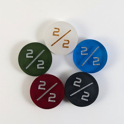 Five 2/2 tokens arranged in a circle face up. White with gold numbers is at the top and blue, black, red, and dark green all with silver numbers follow going clockwise.