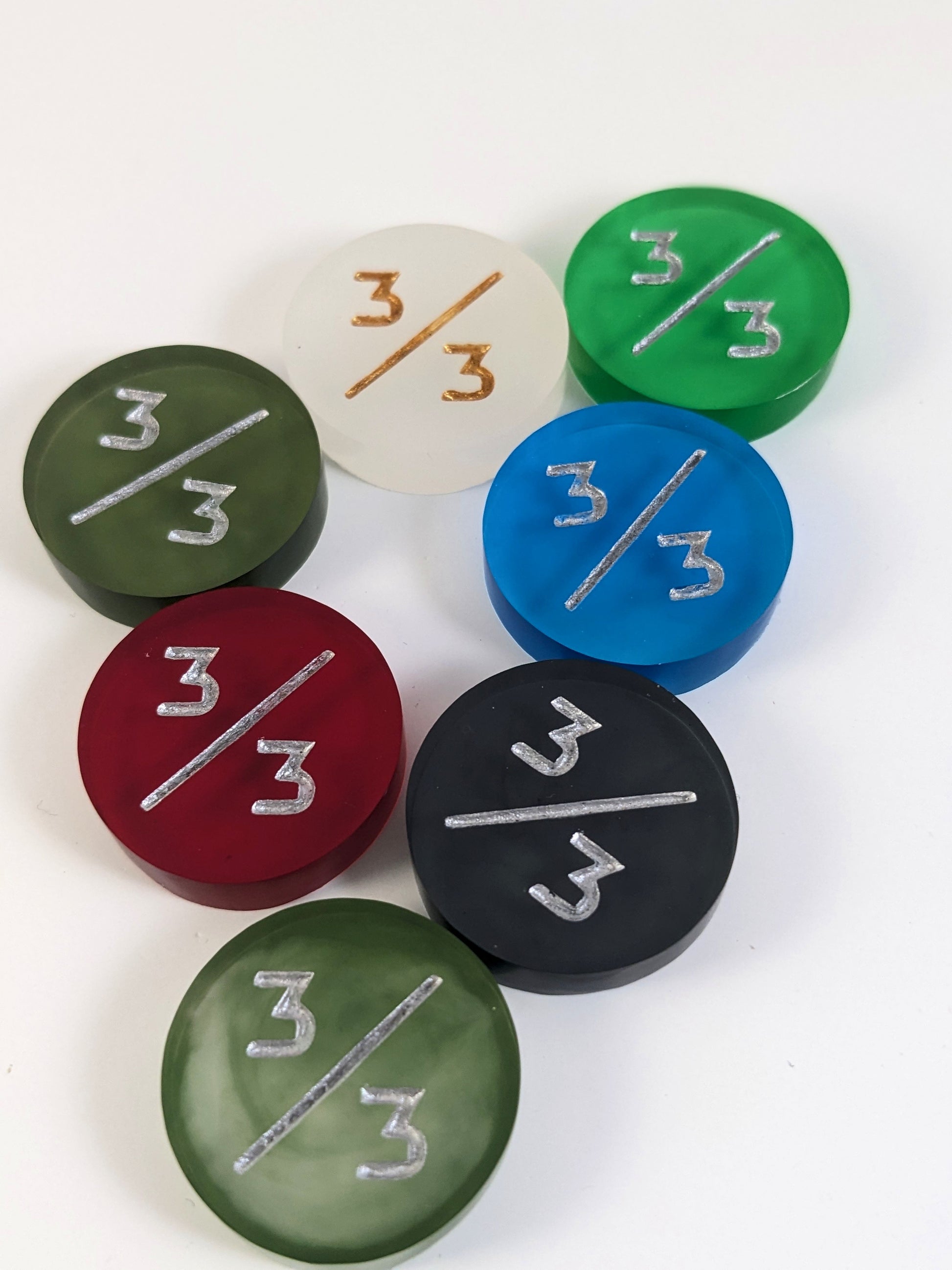 A collection of 3/3 tokens in a variety of colors on a white background. Each token is face up.