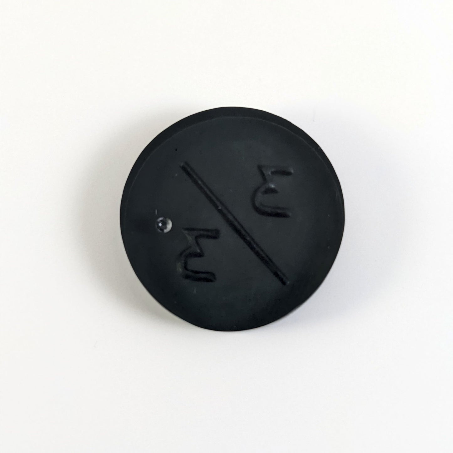 A top down photo of the back of a black 3/3 token with silver numbers sitting on a white background. A bubble is visible.