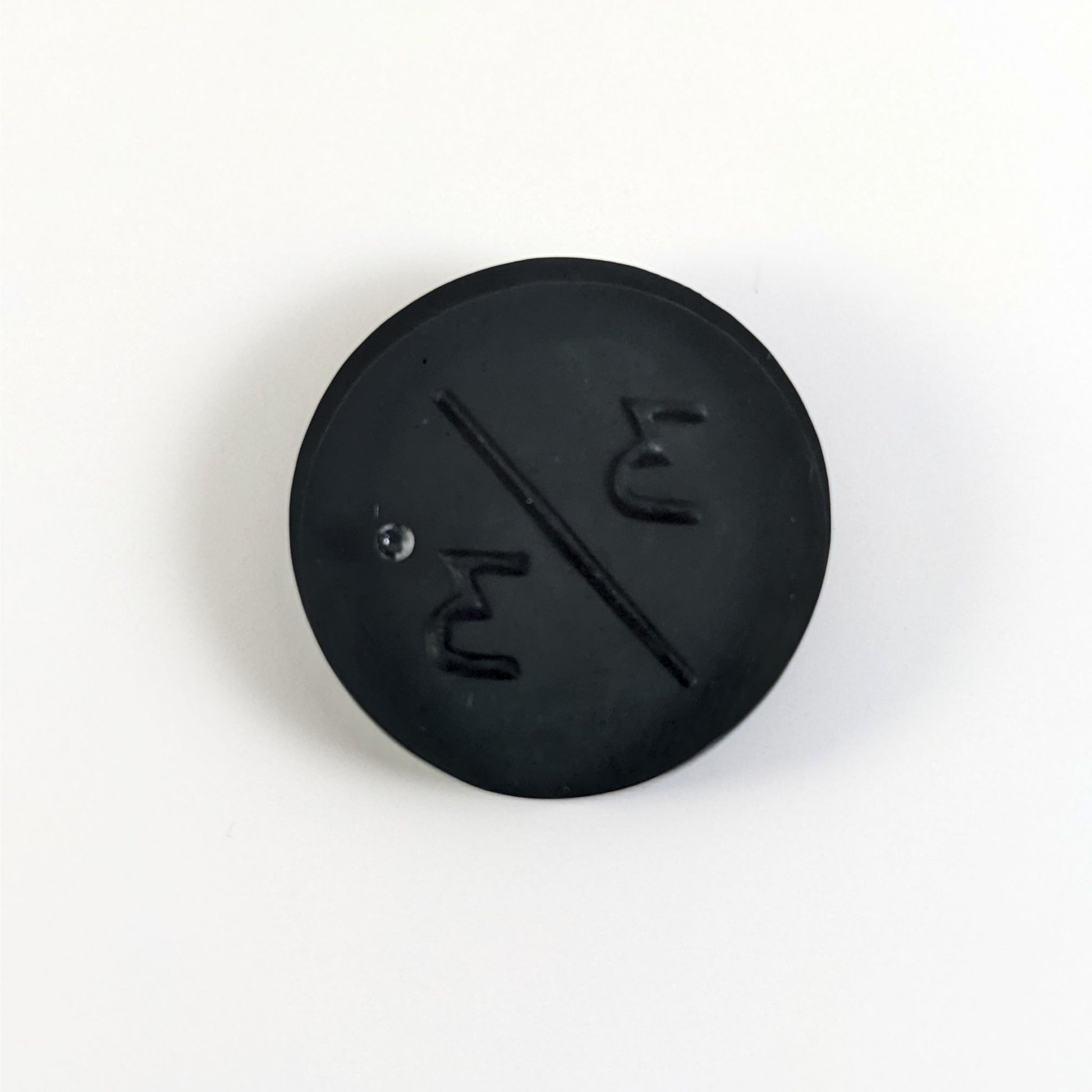A top down photo of the back of a black 3/3 token with silver numbers sitting on a white background. A bubble is visible.
