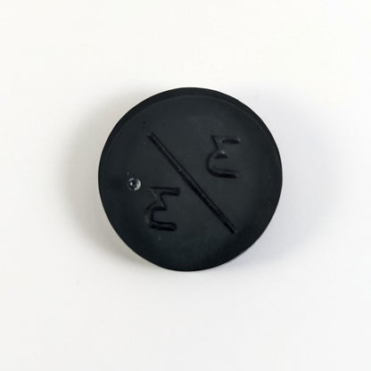 A top down photo of the back of a black 3/3 token with silver numbers sitting on a white background. A bubble is visible.