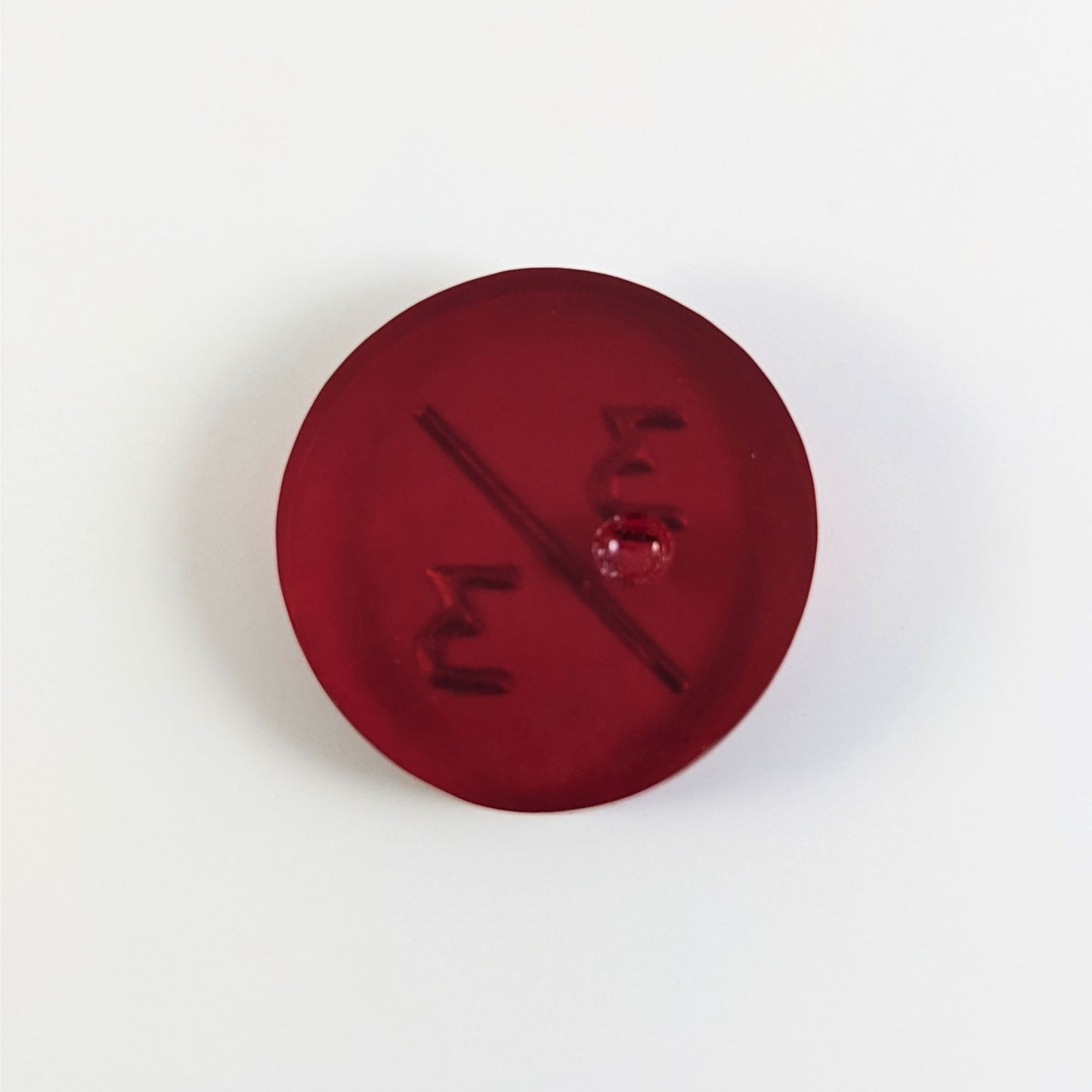 A top down photo of the back of a red 3/3 token with silver numbers sitting on a white background. A bubble is visible.
