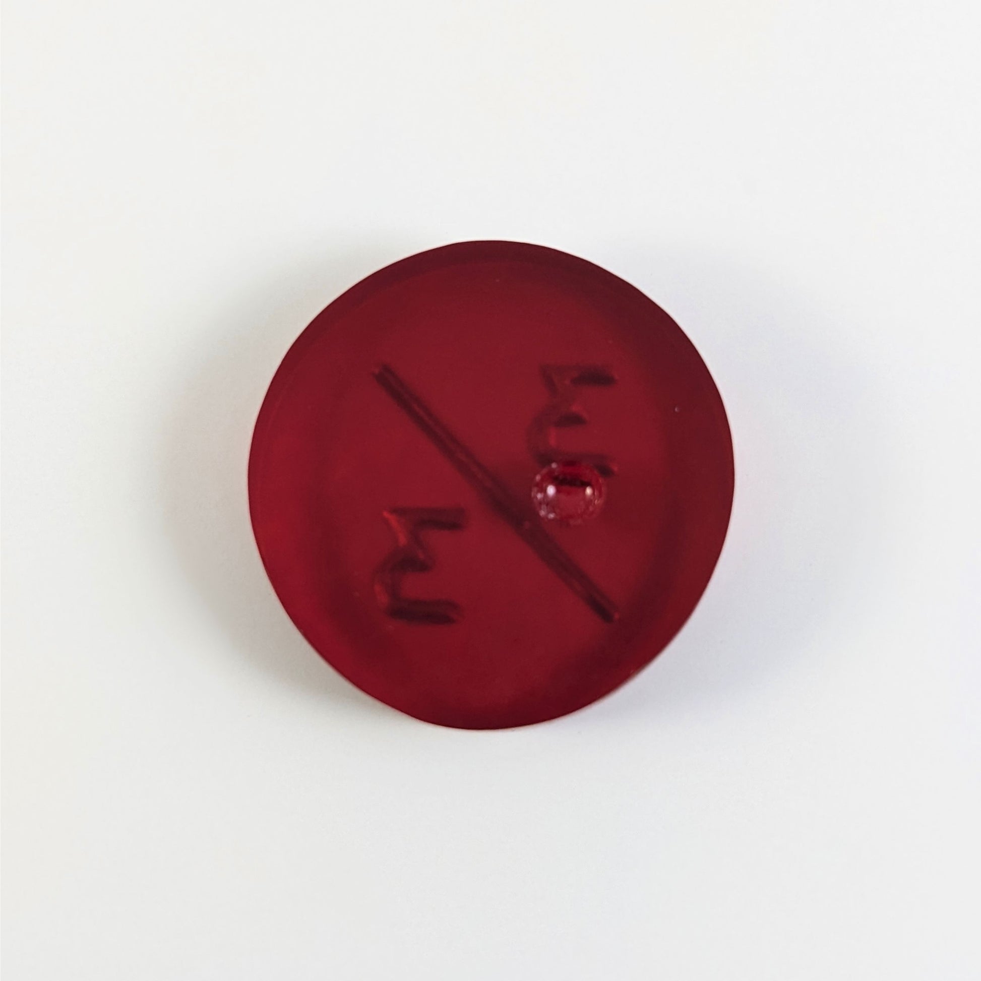A top down photo of the back of a red 3/3 token with silver numbers sitting on a white background. A bubble is visible.