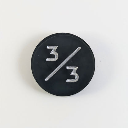 A top down photo of a black 3/3 token with silver numbers sits on a white background.