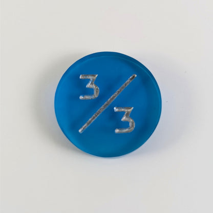 A top down photo of a blue 3/3 token with silver numbers sits on a white background.
