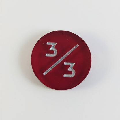A top down photo of a red 3/3 token with silver numbers sits on a white background.