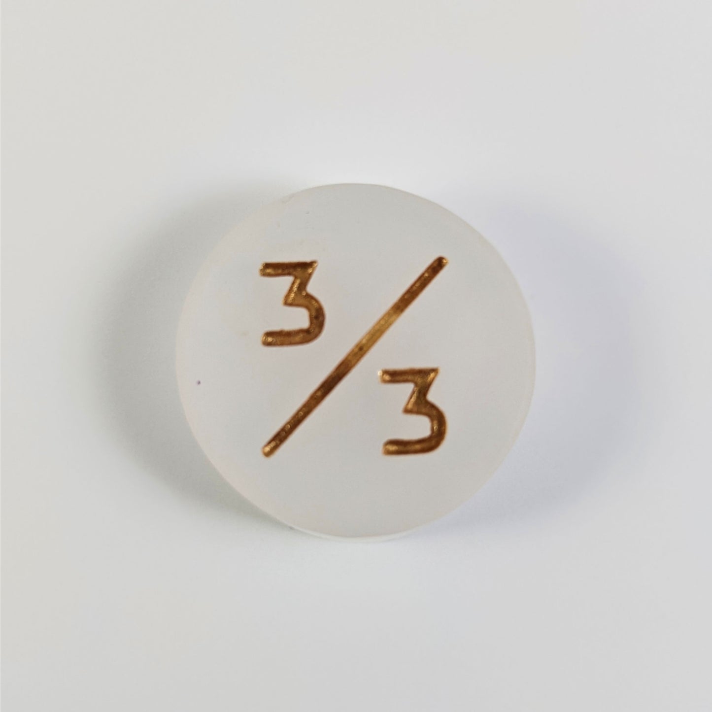 A top down photo of a white 3/3 token with gold numbers sits on a white background.