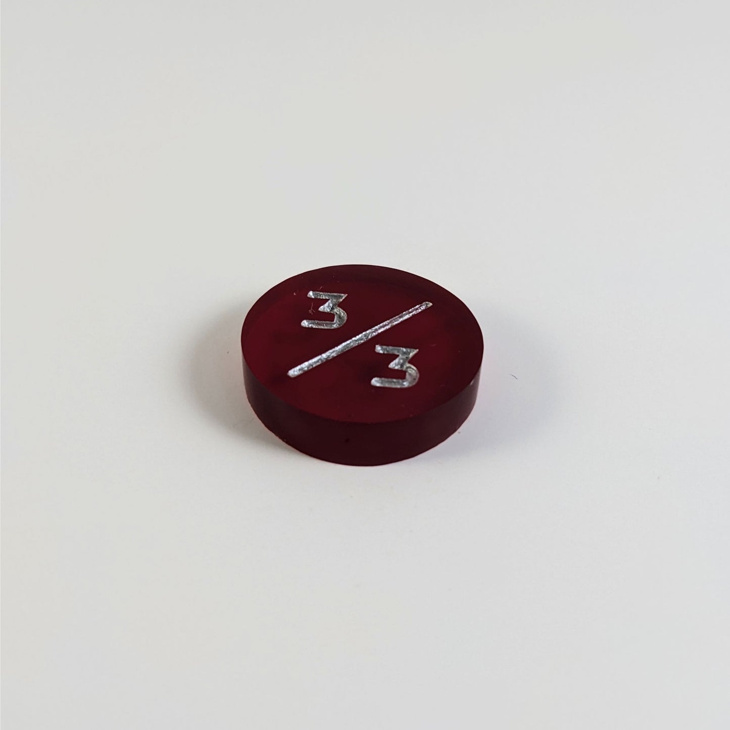 A low angle photo of a red 3/3 token with silver numbers sits on a white background.