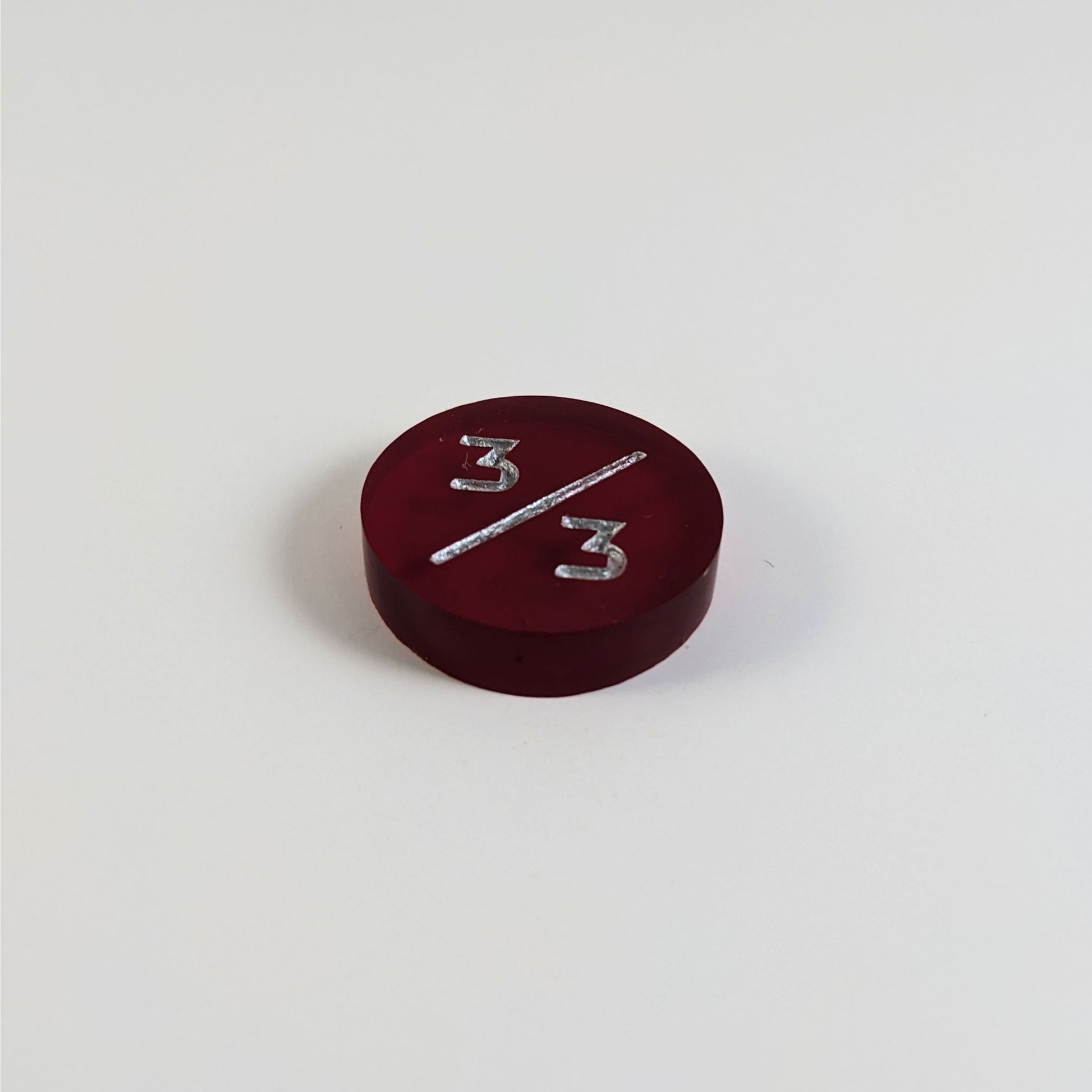 A low angle photo of a red 3/3 token with silver numbers sits on a white background.
