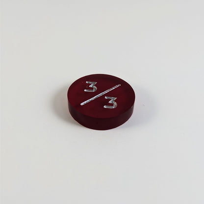 A low angle photo of a red 3/3 token with silver numbers sits on a white background.