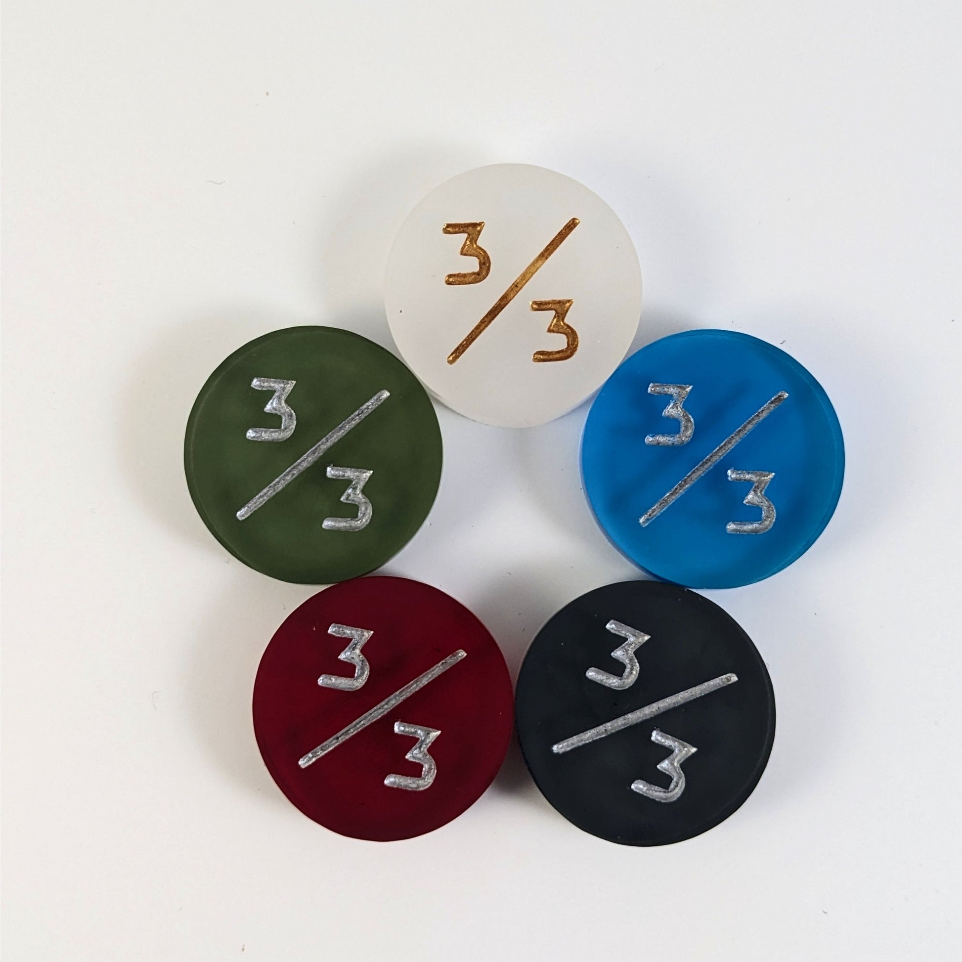 Five 3/3 tokens arranged in a circle face up. White with gold numbers is at the top and blue, black, red, and dark green all with silver numbers follow going clockwise.