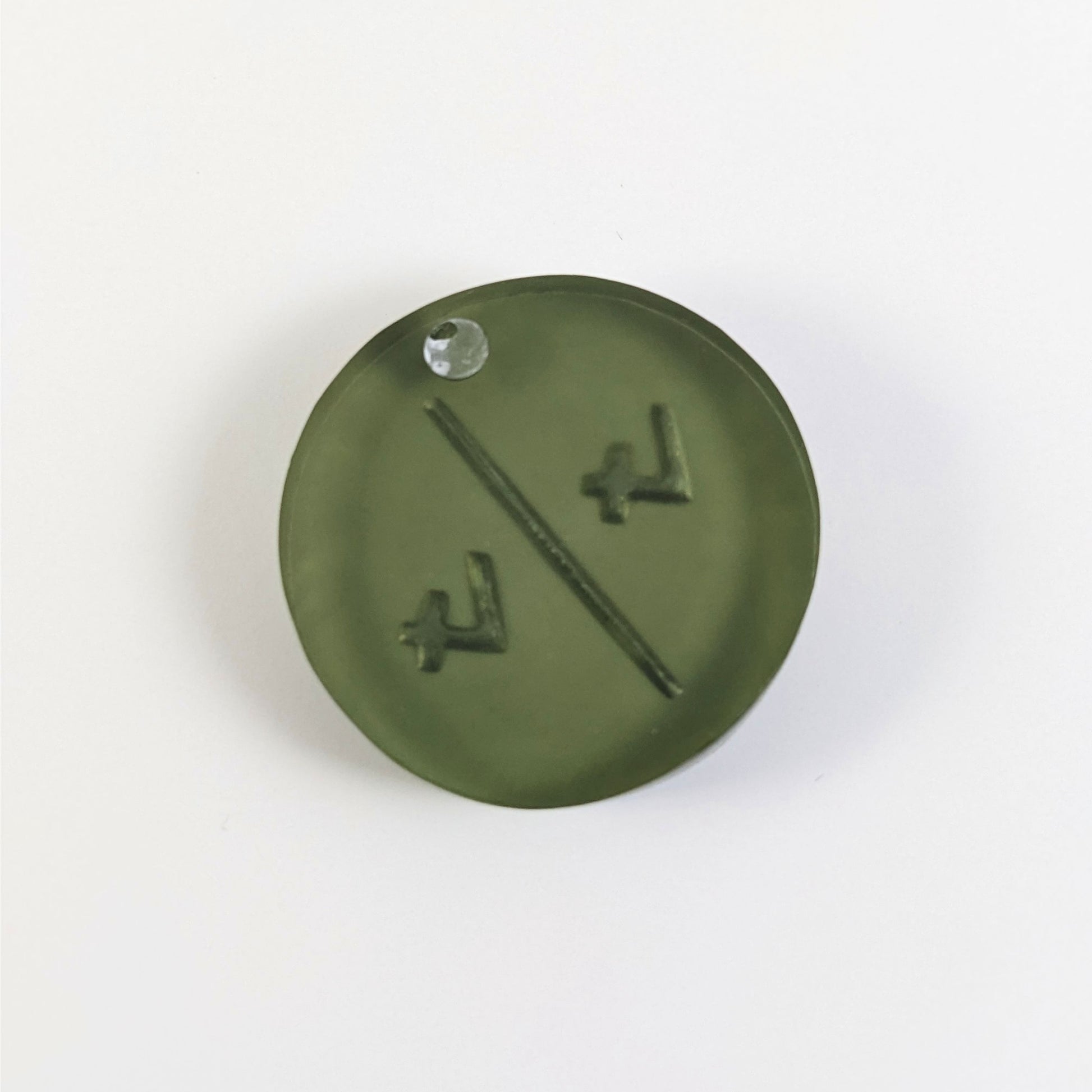 A top down photo of the back of a dark green 4/4 token with silver numbers sitting on a white background. A bubble is visible.