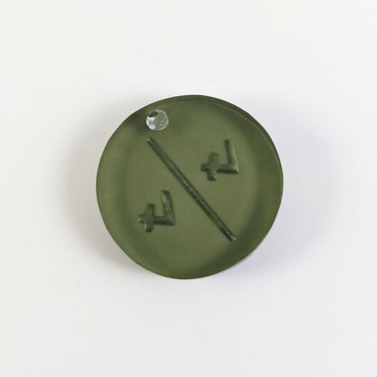 A top down photo of the back of a dark green 4/4 token with silver numbers sitting on a white background. A bubble is visible.