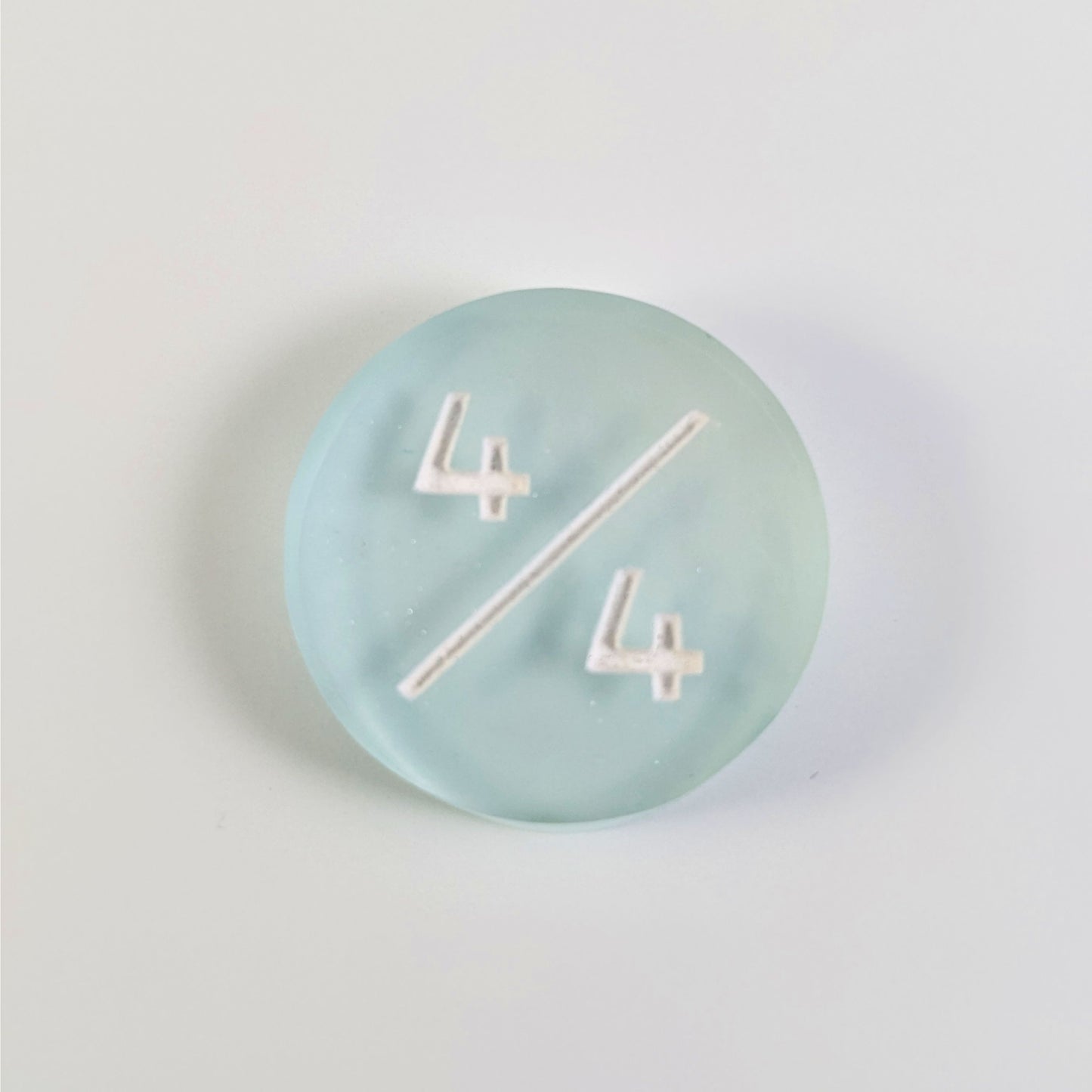 A top down photo of a frosty white and blue 4/4 token with white numbers sits on a white background. The cosmetic flaw is not visible from this angle.