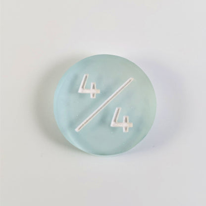 A top down photo of a frosty white and blue 4/4 token with white numbers sits on a white background. The cosmetic flaw is not visible from this angle.