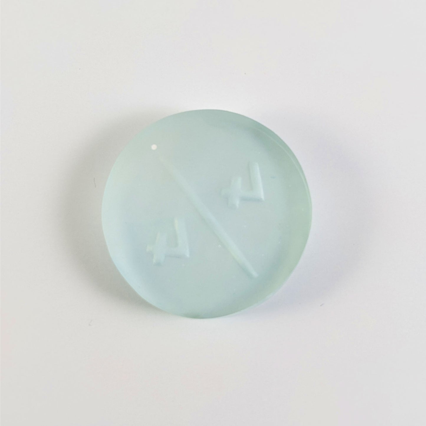 A top down photo of the back of a frosty white and blue 4/4 token with white numbers sitting on a white background. A bubble is visible.