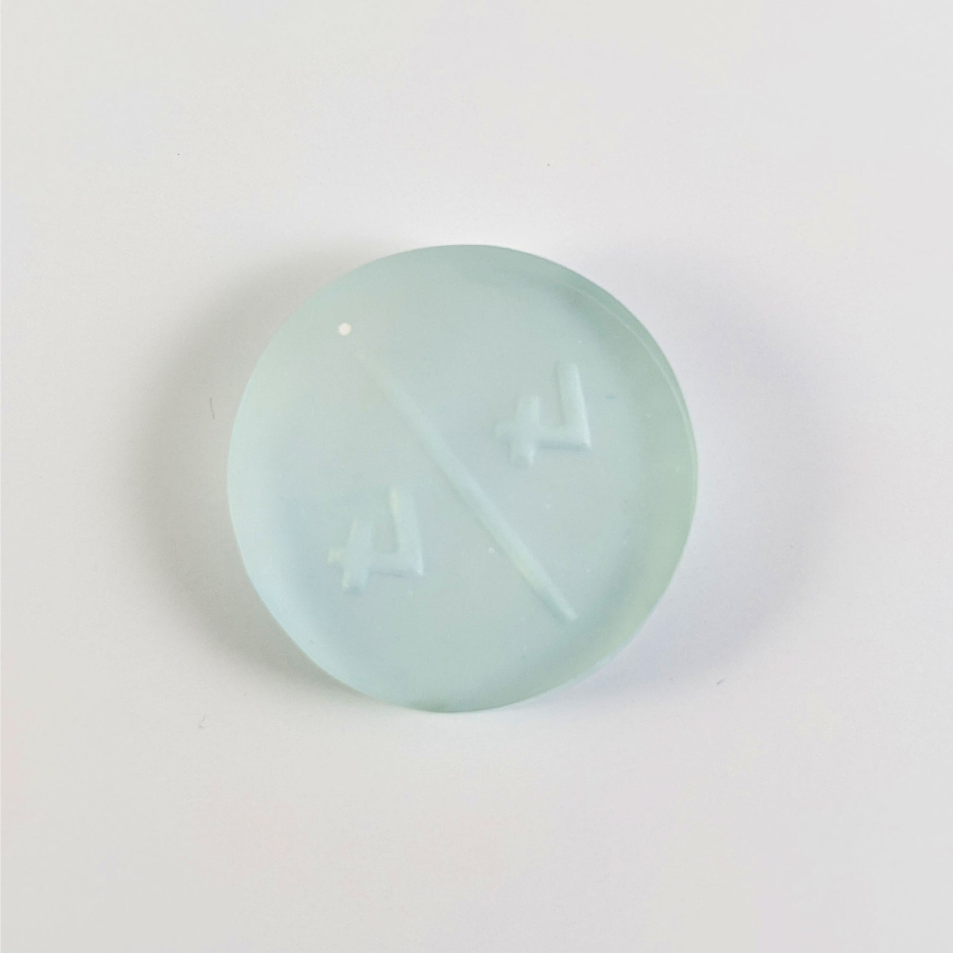 A top down photo of the back of a frosty white and blue 4/4 token with white numbers sitting on a white background. A bubble is visible.