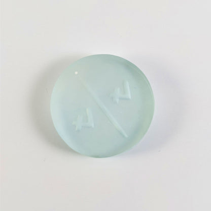 A top down photo of the back of a frosty white and blue 4/4 token with white numbers sitting on a white background. A bubble is visible.