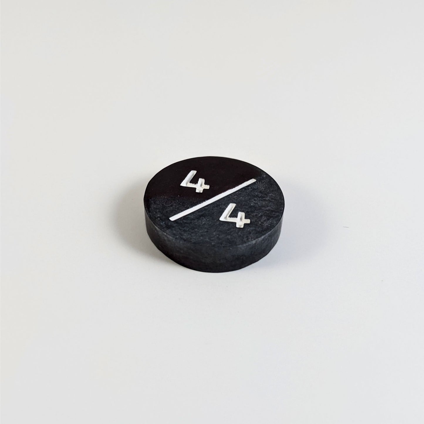 A low angle photo of a silver and maroon 4/4 token with white numbers sits on a white background. The cosmetic flaw is not apparently visible at this angle.