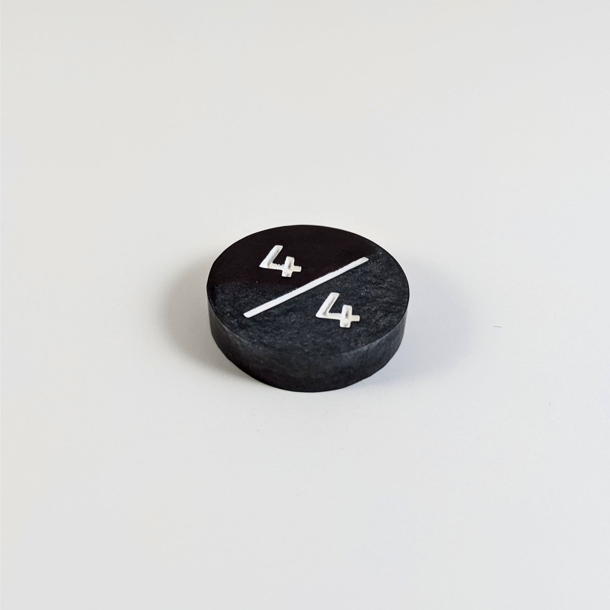 A low angle photo of a silver and maroon 4/4 token with white numbers sits on a white background. The cosmetic flaw is not apparently visible at this angle.