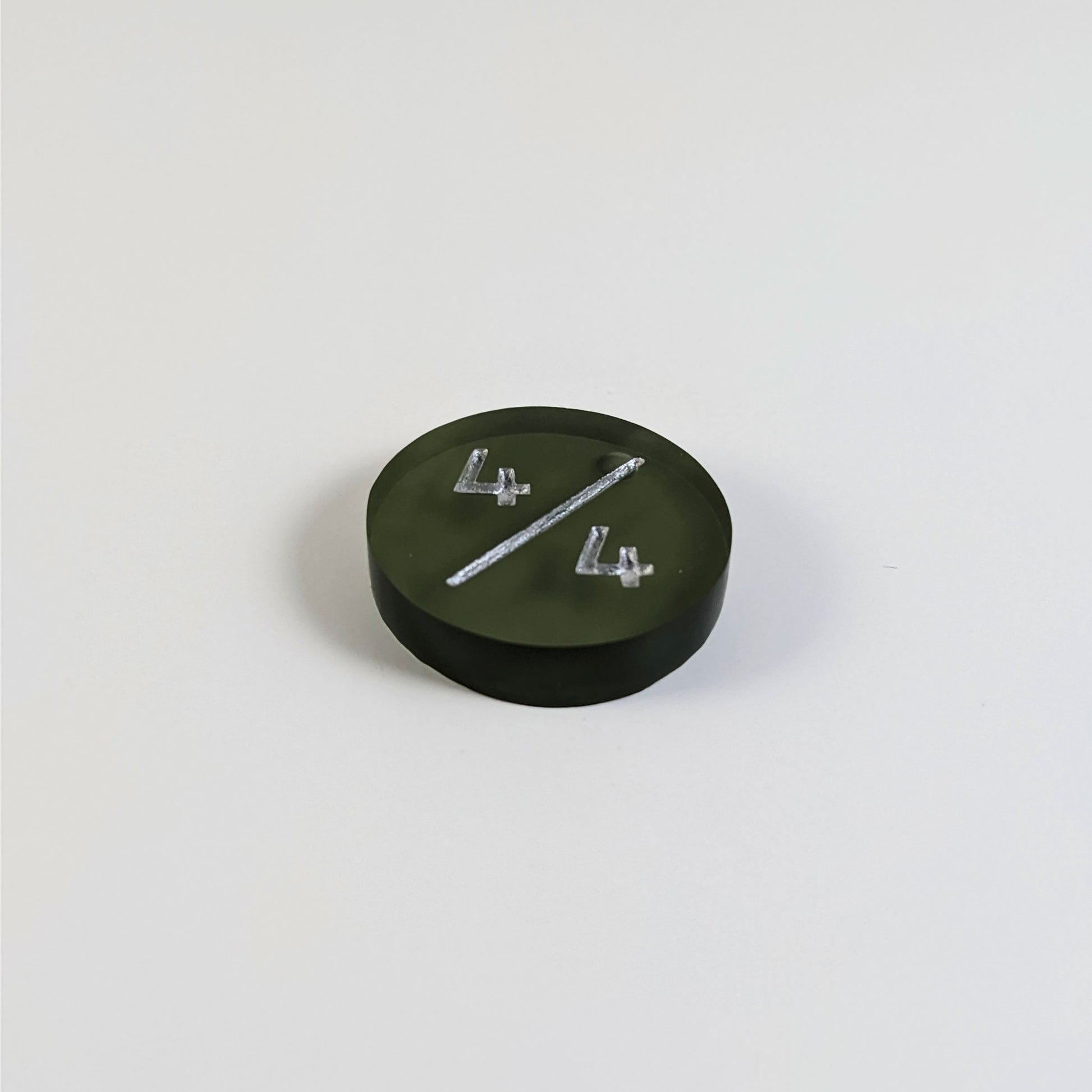 A low angle photo of a dark green 4/4 token with silver numbers sits on a white background. The bubble is visible at the top part of the slash and is on the back of the token.
