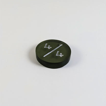 A low angle photo of a dark green 4/4 token with silver numbers sits on a white background. The bubble is visible at the top part of the slash and is on the back of the token.