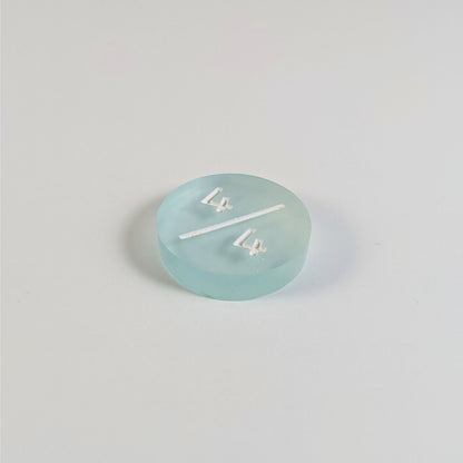 A low angle photo of a frosty white and blue 4/4 token with white numbers sits on a white background. The cosmetic flaw is not apparently visible at this angle.