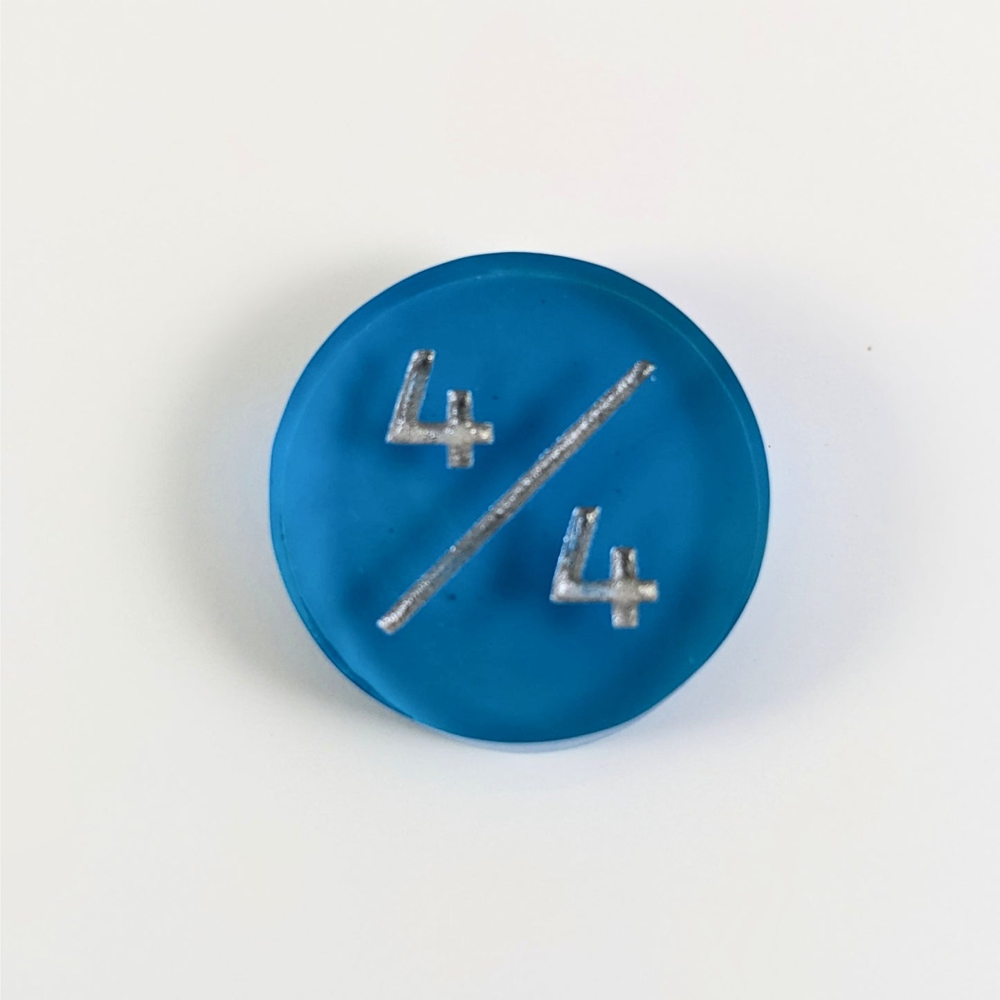 A top down photo of a blue 4/4 token with silver numbers sits on a white background.