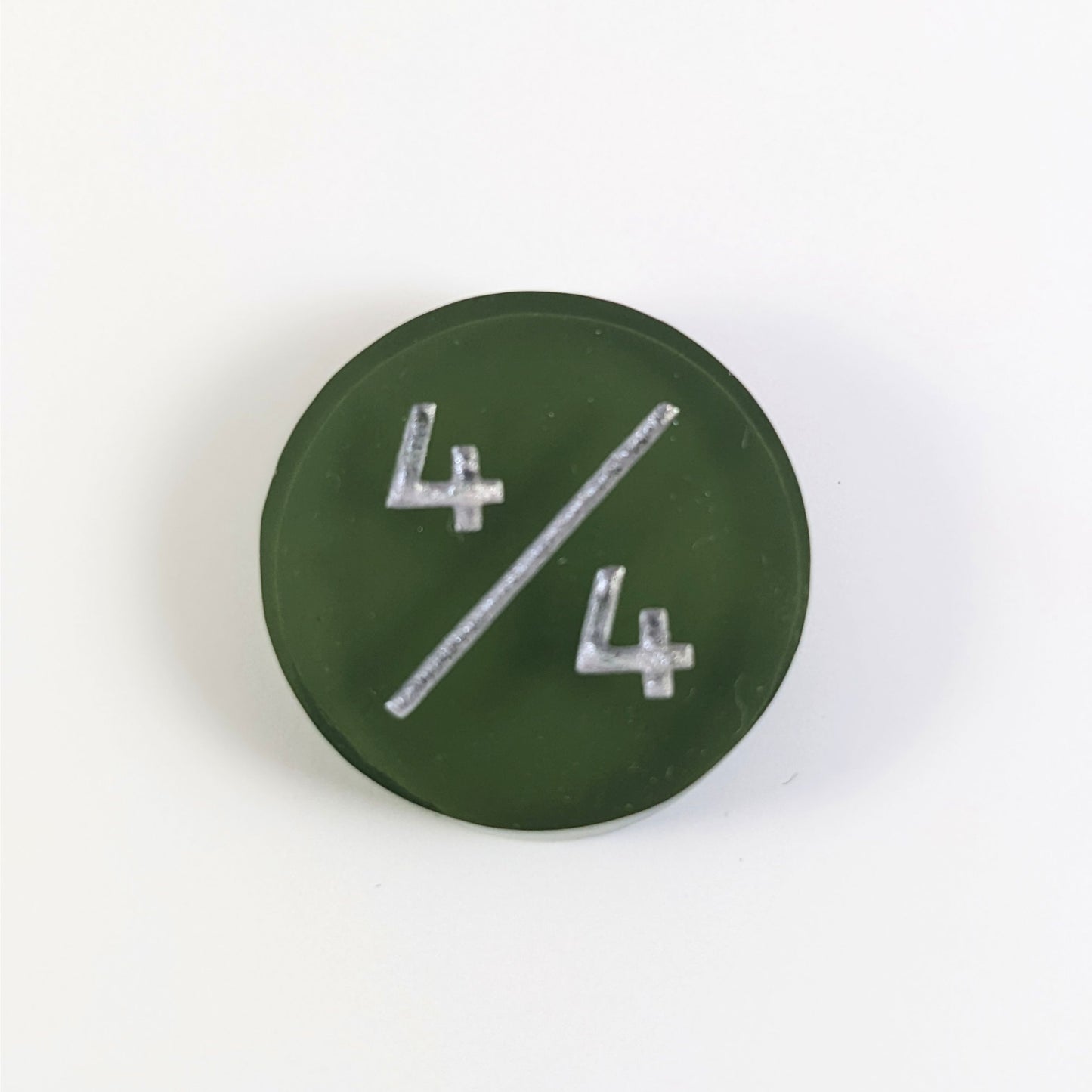 A top down photo of a dark green 4/4 token with silver numbers sits on a white background.