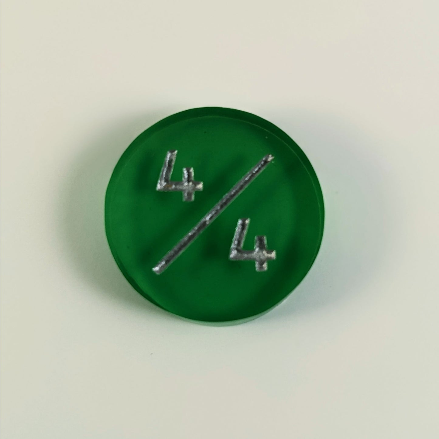 A top down photo of a green 4/4 token with silver numbers sits on a white background.
