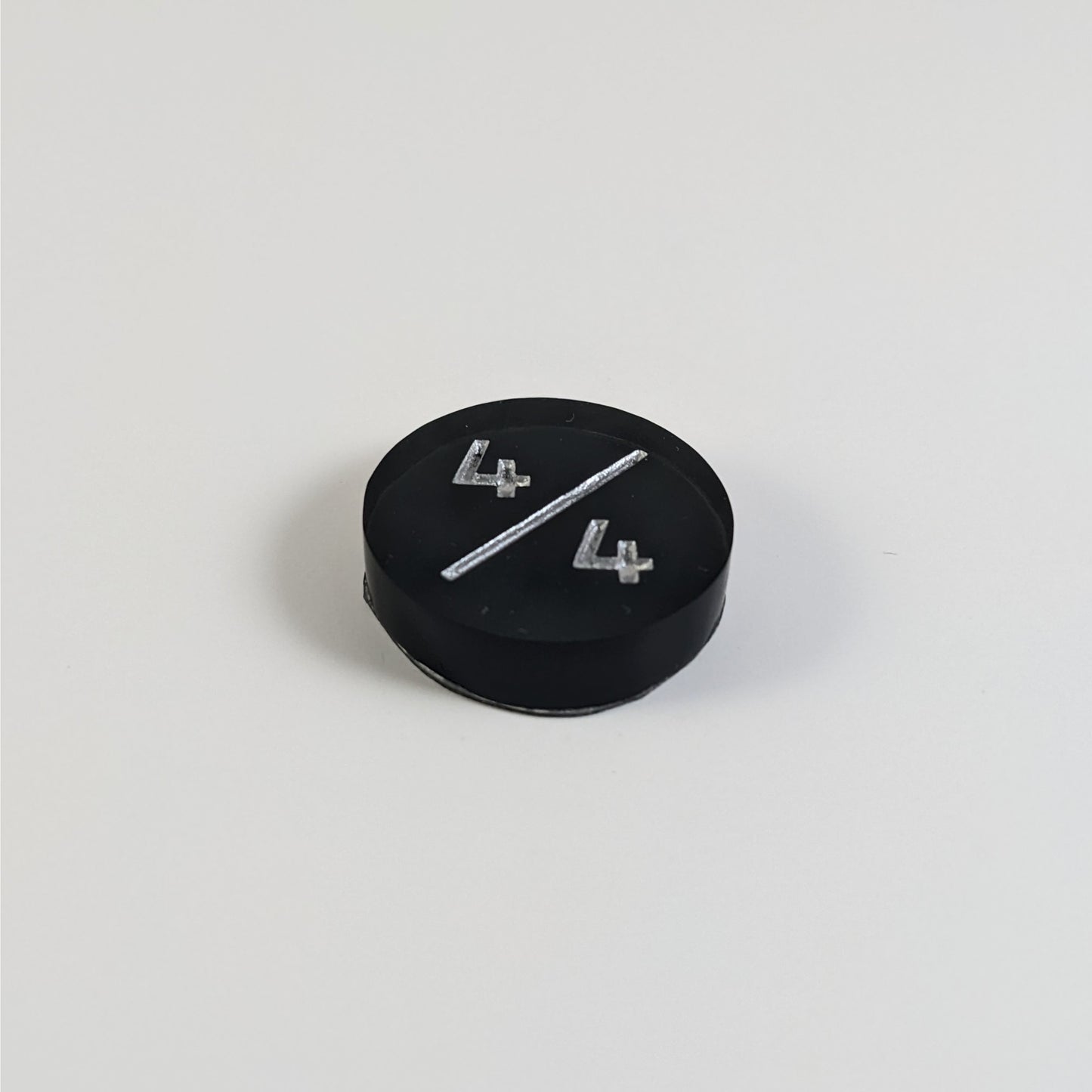 A low angle photo of a black 4/4 token with silver numbers sits on a white background.