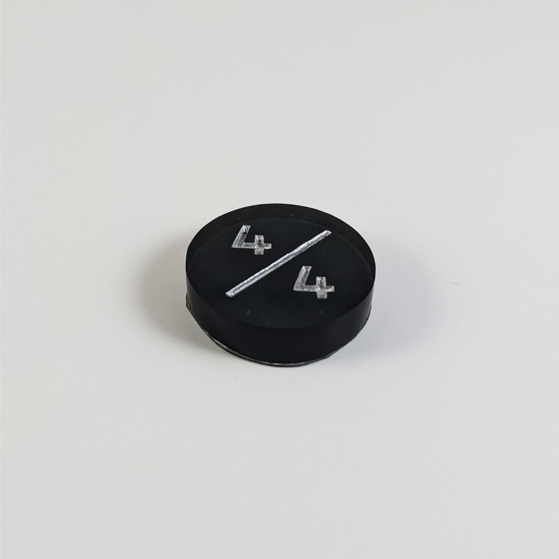 A low angle photo of a black 4/4 token with silver numbers sits on a white background.