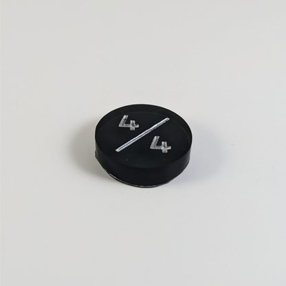 A low angle photo of a black 4/4 token with silver numbers sits on a white background.