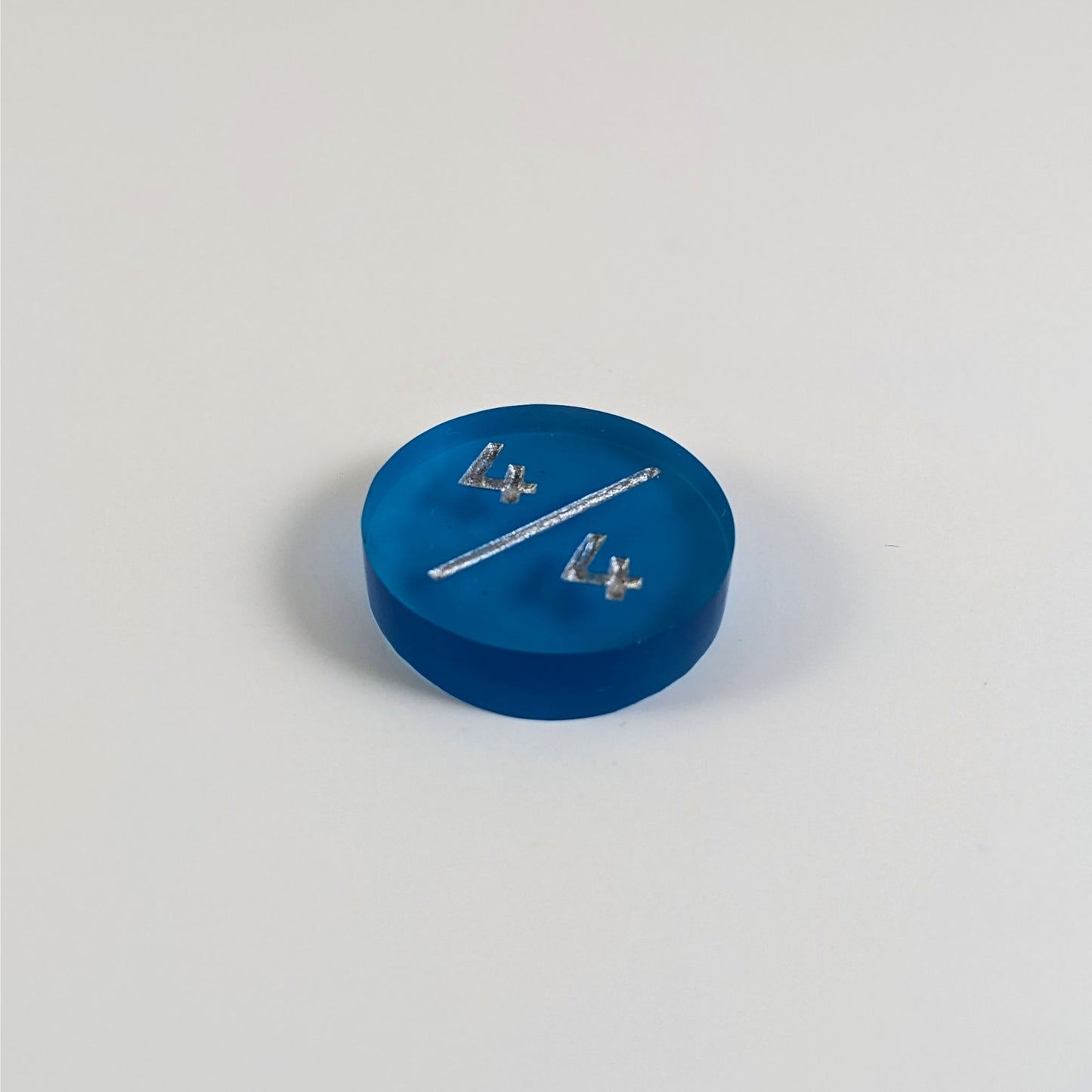 A low angle photo of a blue 4/4 token with silver numbers sits on a white background.