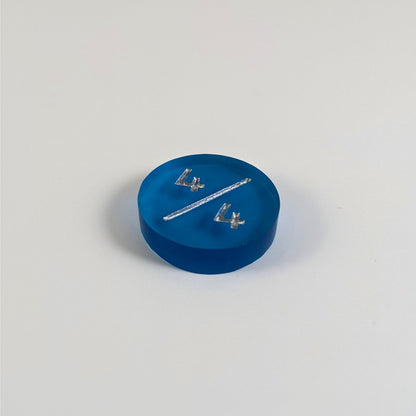 A low angle photo of a blue 4/4 token with silver numbers sits on a white background.