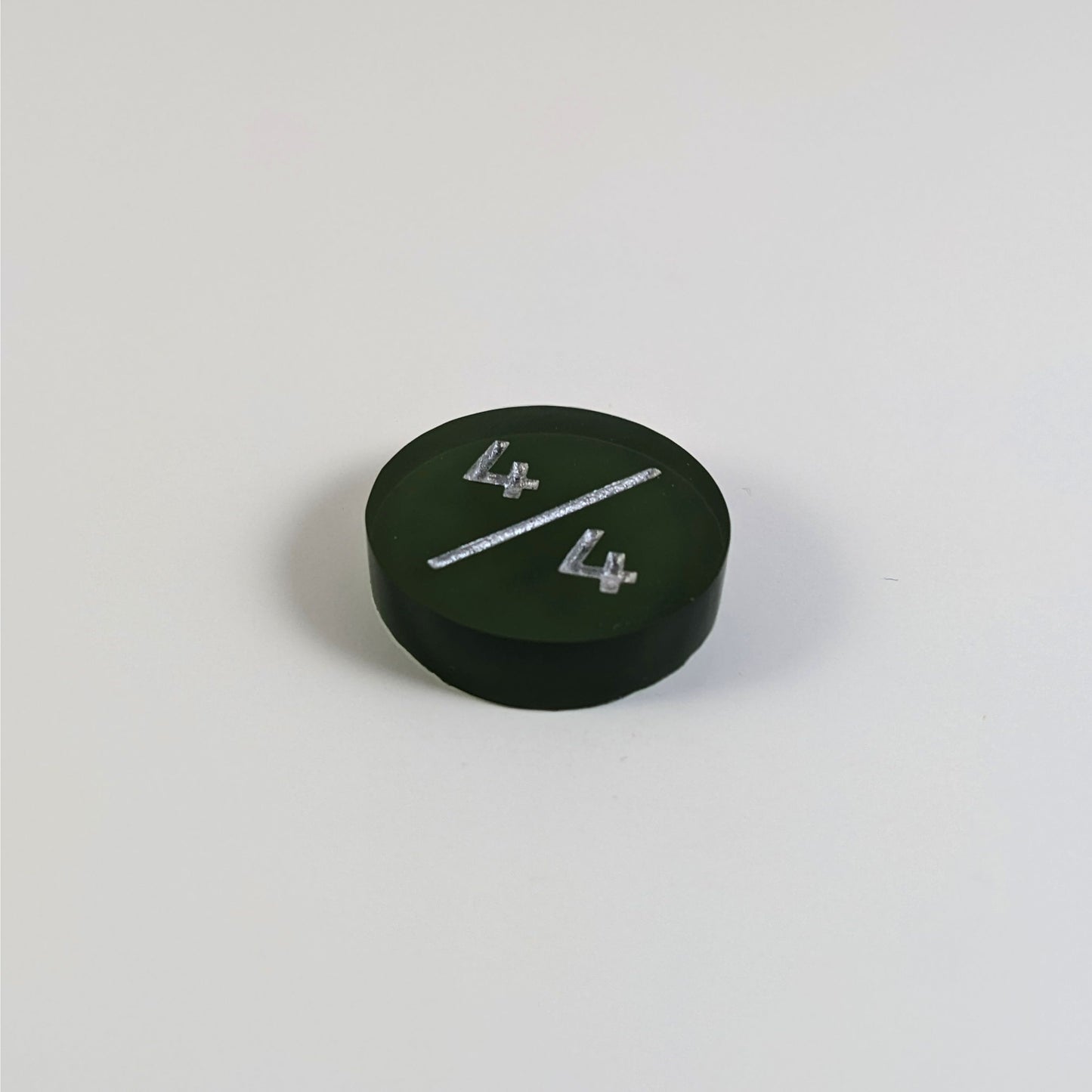A low angle photo of a dark green 4/4 token with silver numbers sits on a white background.