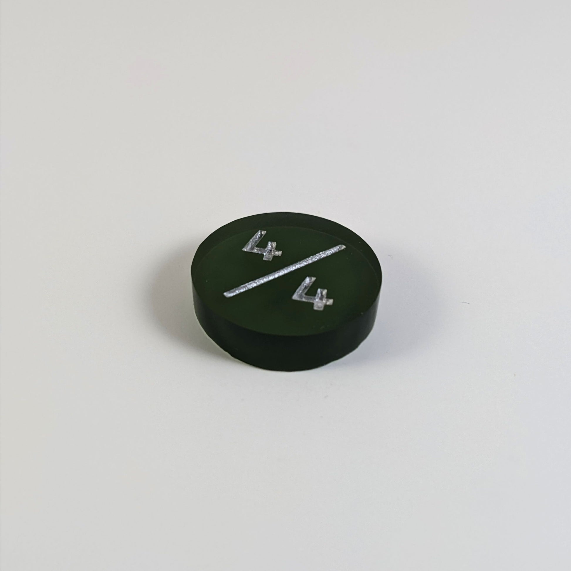 A low angle photo of a dark green 4/4 token with silver numbers sits on a white background.