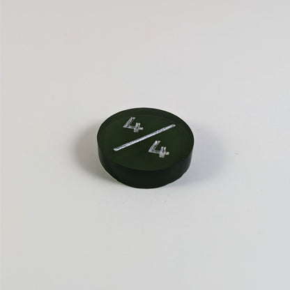 A low angle photo of a dark green 4/4 token with silver numbers sits on a white background.
