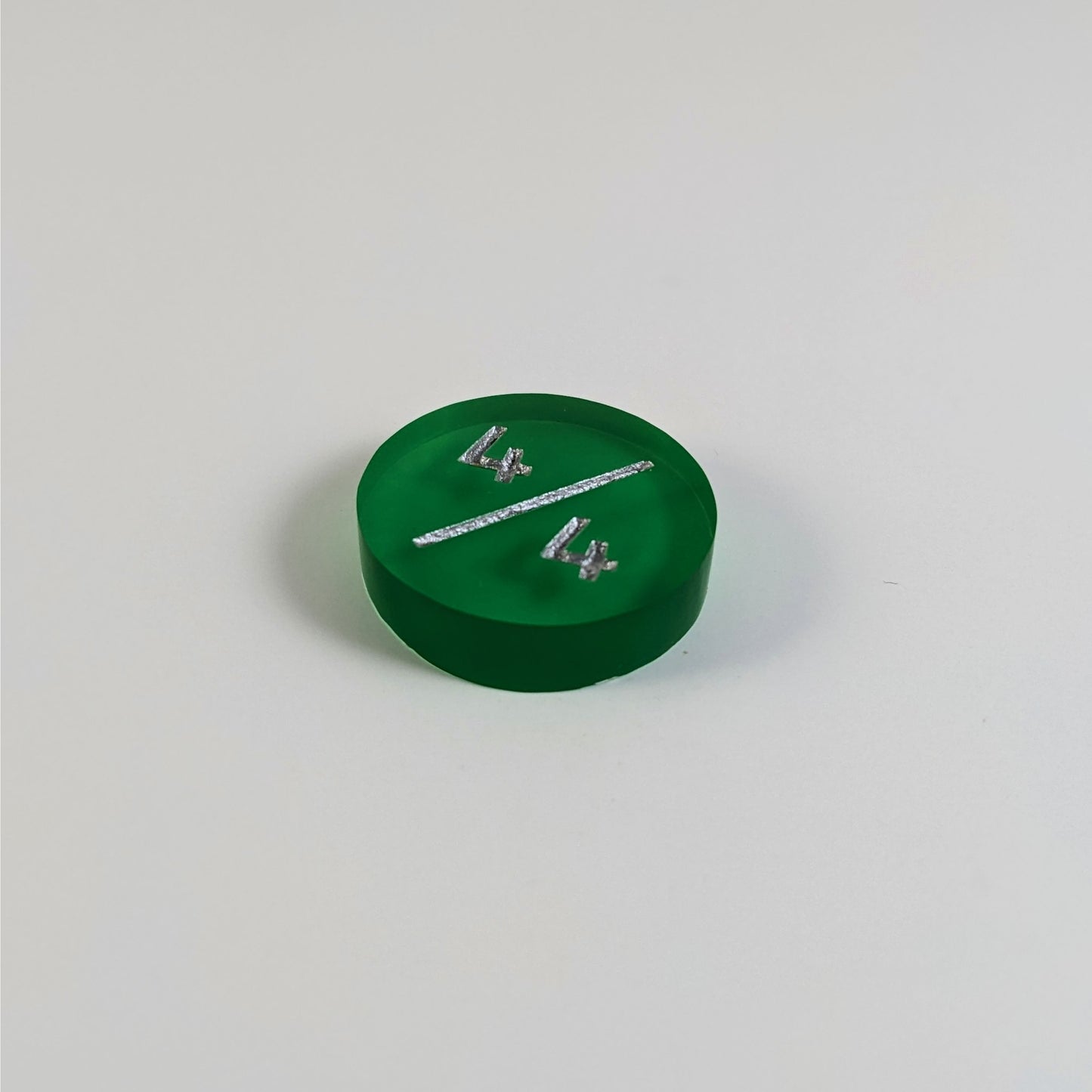A low angle photo of a green 4/4 token with silver numbers sits on a white background.