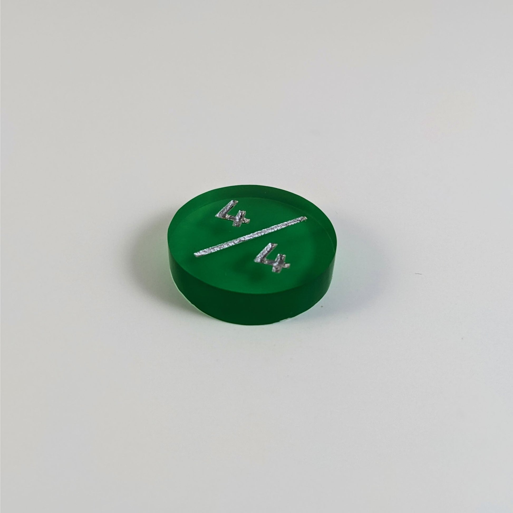 A low angle photo of a green 4/4 token with silver numbers sits on a white background.