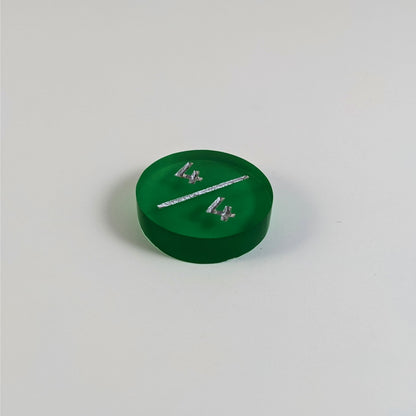 A low angle photo of a green 4/4 token with silver numbers sits on a white background.