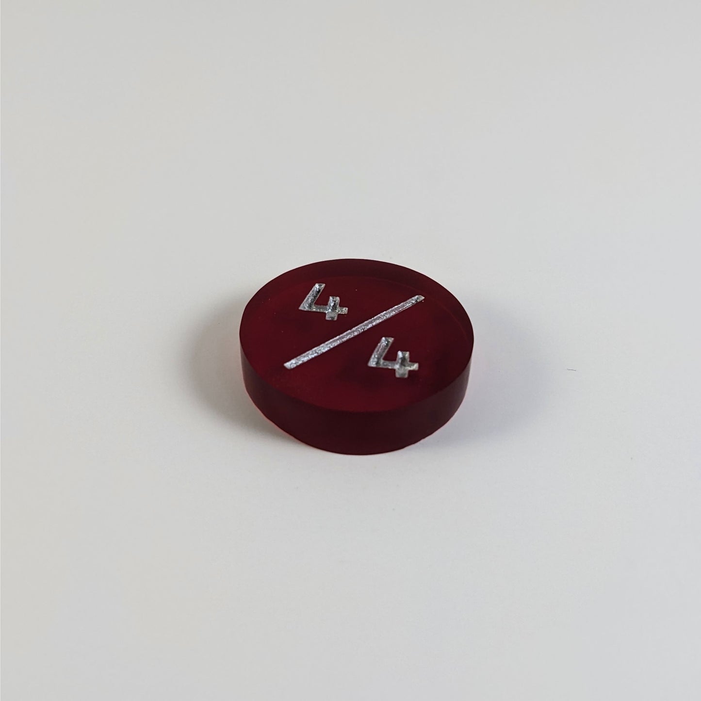 A low angle photo of a red 4/4 token with silver numbers sits on a white background.