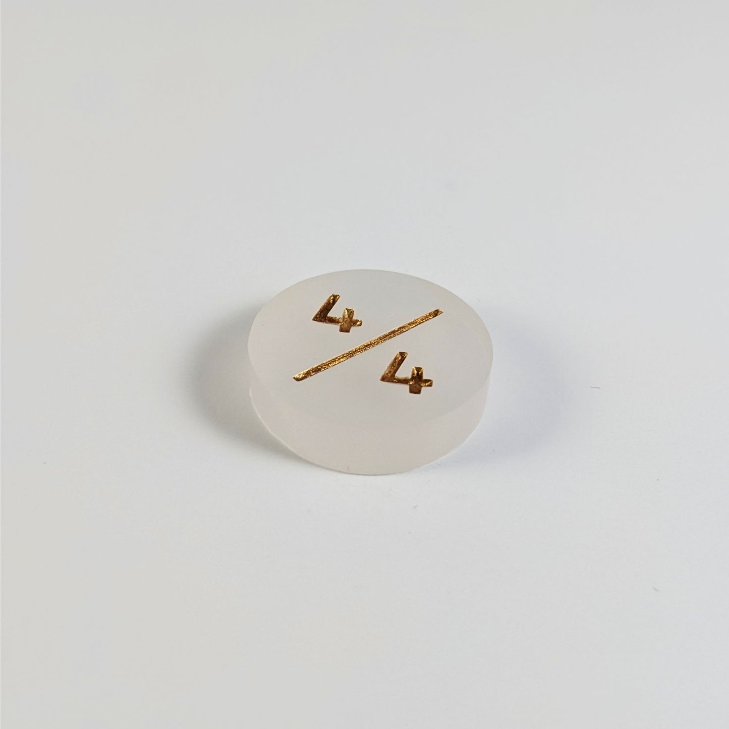 A low angle photo of a white 4/4 token with gold numbers sits on a white background.