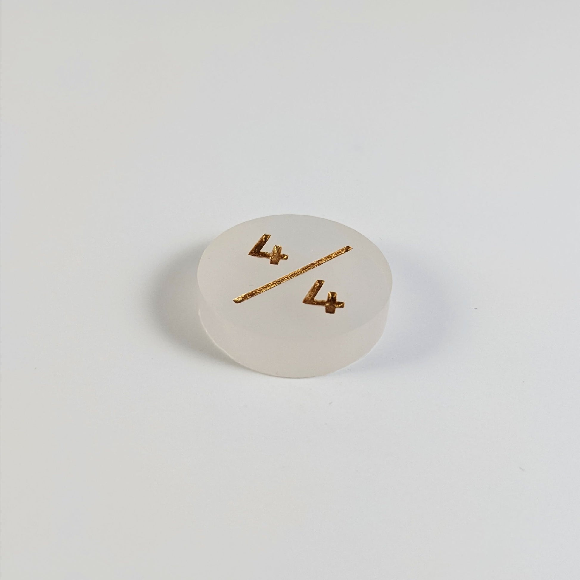 A low angle photo of a white 4/4 token with gold numbers sits on a white background.