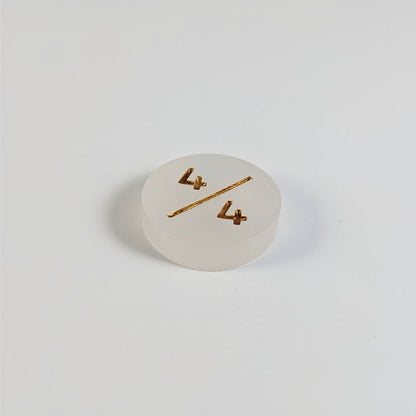 A low angle photo of a white 4/4 token with gold numbers sits on a white background.
