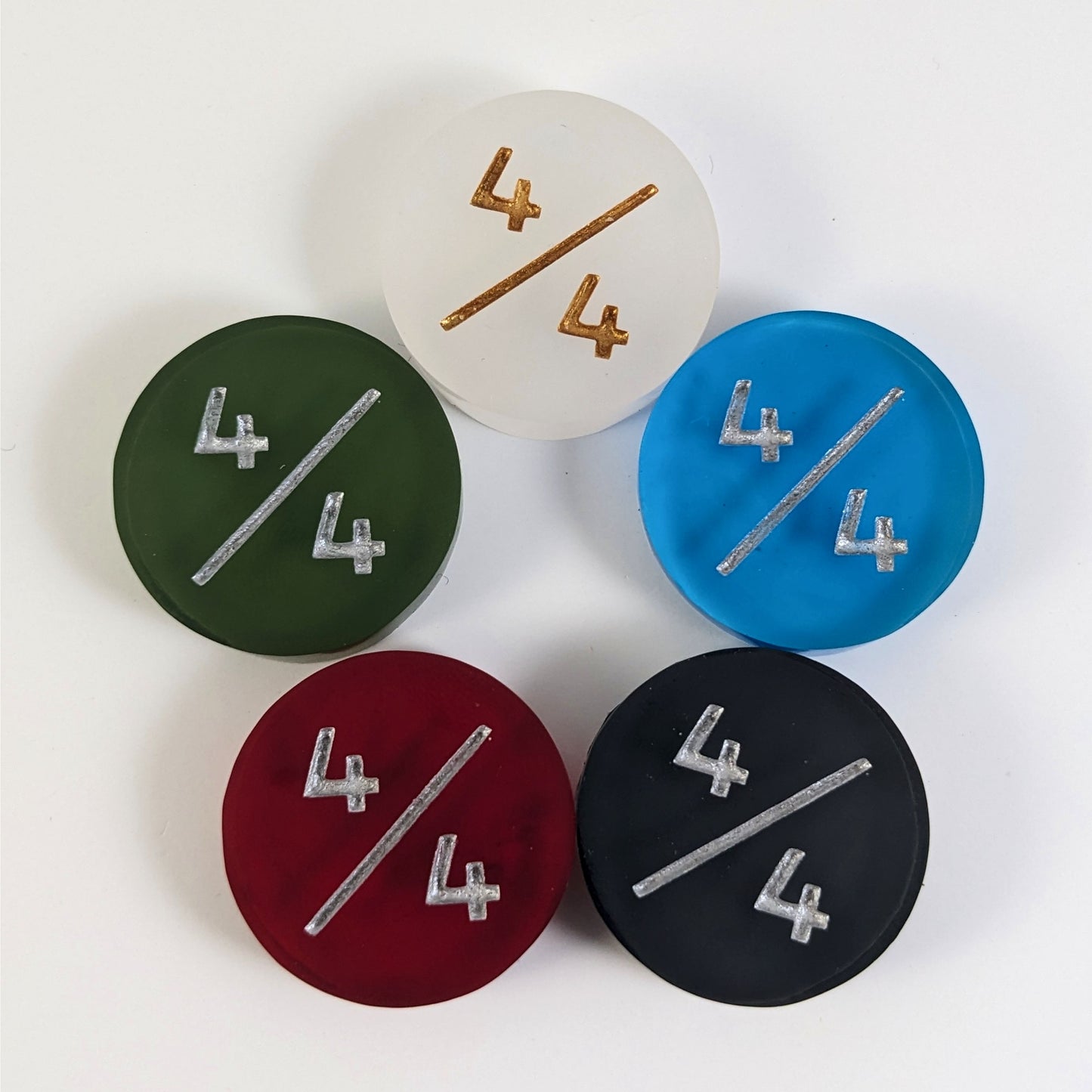 Five 4/4 tokens arranged in a circle face up. White with gold numbers is at the top and blue, black, red, and dark green all with silver numbers follow going clockwise.