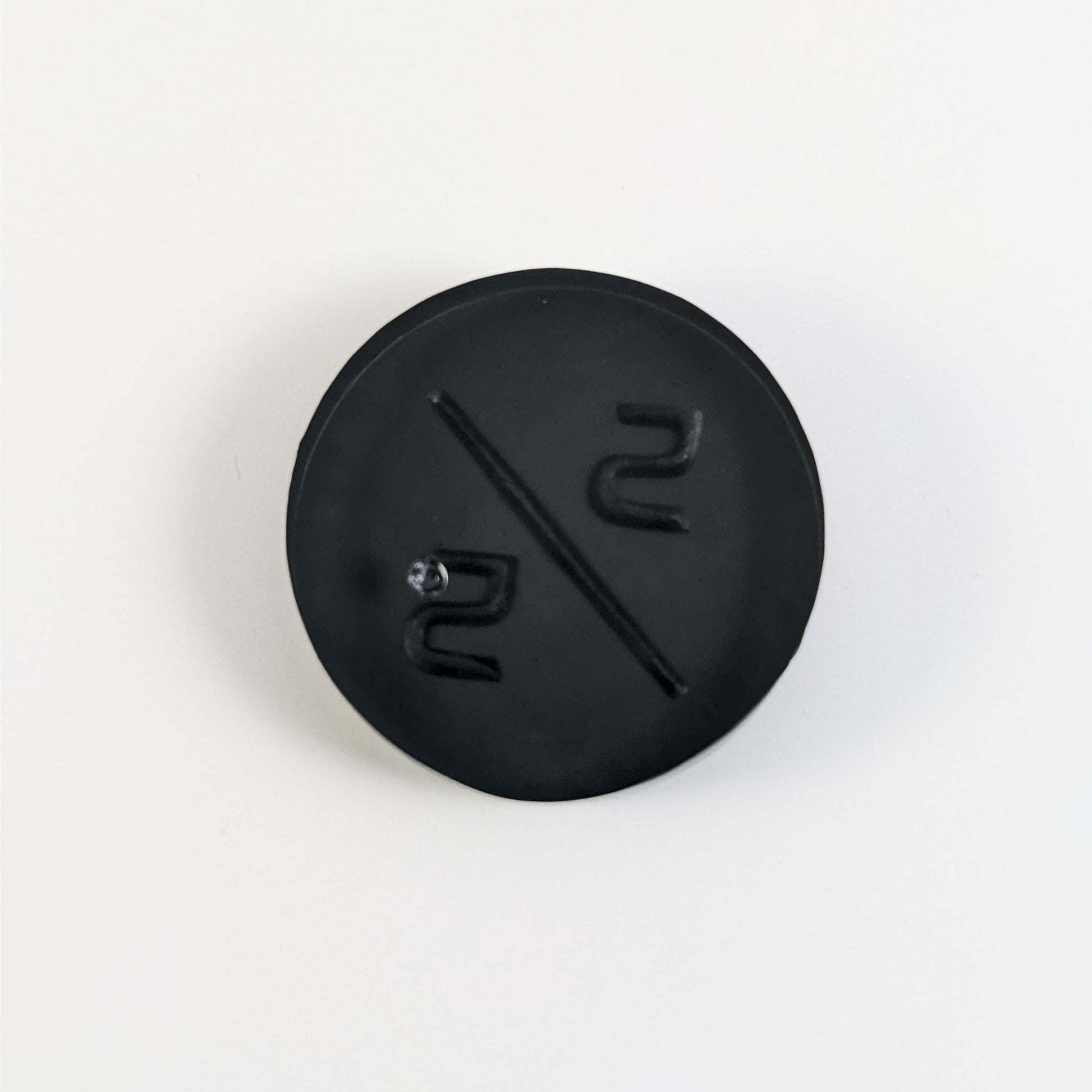 A top down photo of the back of a black 5/5 token with silver numbers sitting on a white background. A bubble is visible.