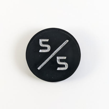 A top down photo of a black 5/5 token with silver numbers sits on a white background.