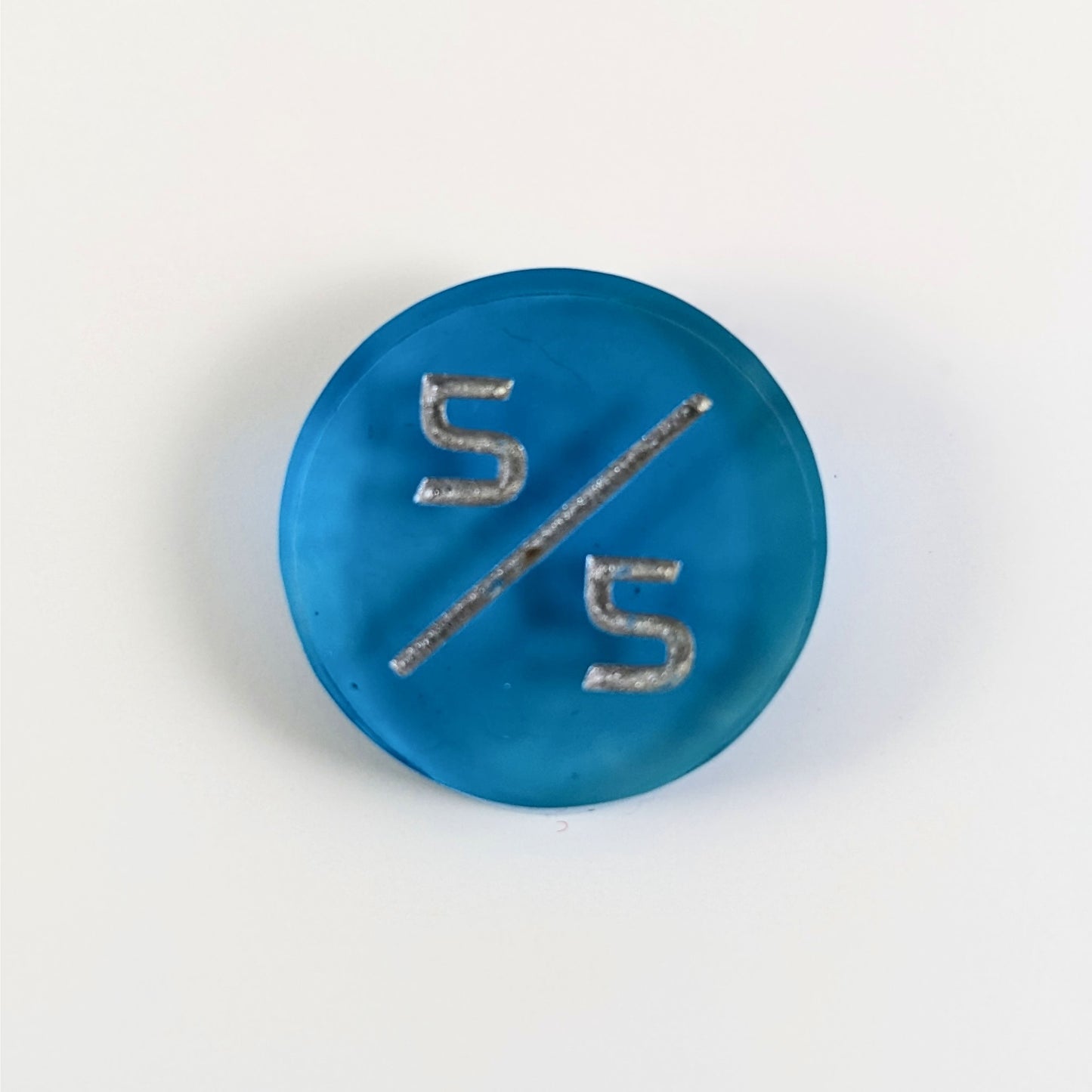 A top down photo of a blue 5/5 token with silver numbers sits on a white background.