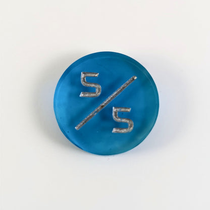 A top down photo of a blue 5/5 token with silver numbers sits on a white background.